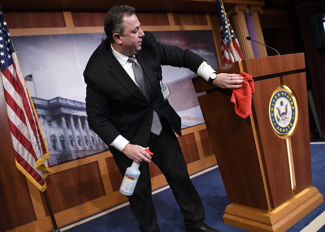 Mike Mastrian, director of the Senate Radio and Television Gallery, cleans down the podium before a news conference with Senate Minority Leader Sen. Chuck Schumer of N.Y., on Capitol Hill in Washington, Tuesday, March 17, 2020. (AP Photo/Susan Walsh)