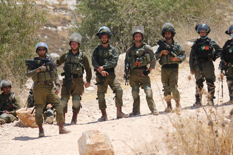 Israeli soldiers watch Palestinians while protesting against a new Israeli settler outpost in the West Bank town of Asira Ash-Shamaliya near Nablus, July 17, 2020. Israeli soldiers prevented the protesters from reaching the outpost site and dispersed the crowd with gas, stun grenades, rubber-coated bullets and live ammunition.