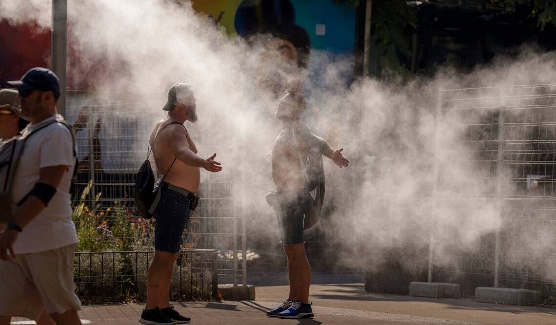 Two men cool themselves with water from a public sprinkler on a hot and sunny day in Barcelona, Spain, July 16, 2022. (AP)